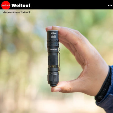 Hand holding a black flashlight with 'Weltool' branding against a blurred natural background