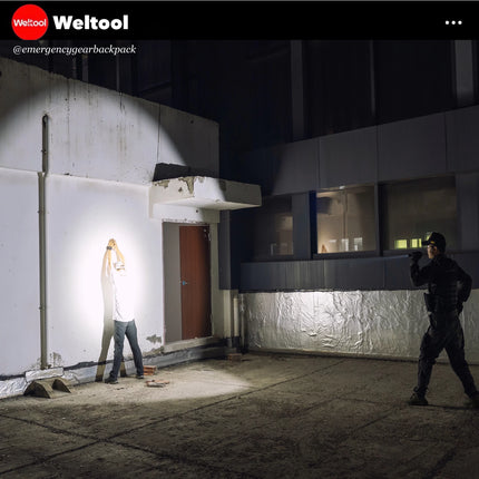 Two people in tactical gear standing outside a building at night, illuminated by a flashlight.