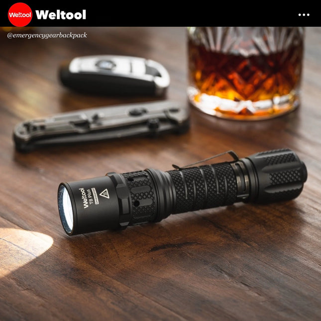 Weltool T8Plus flashlight on a wooden surface with a glass of whiskey and car keys in the background, featuring the Weltool brand.